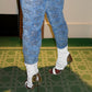 Person wearing blue patterned pants and high-heeled shoes on a green carpet.