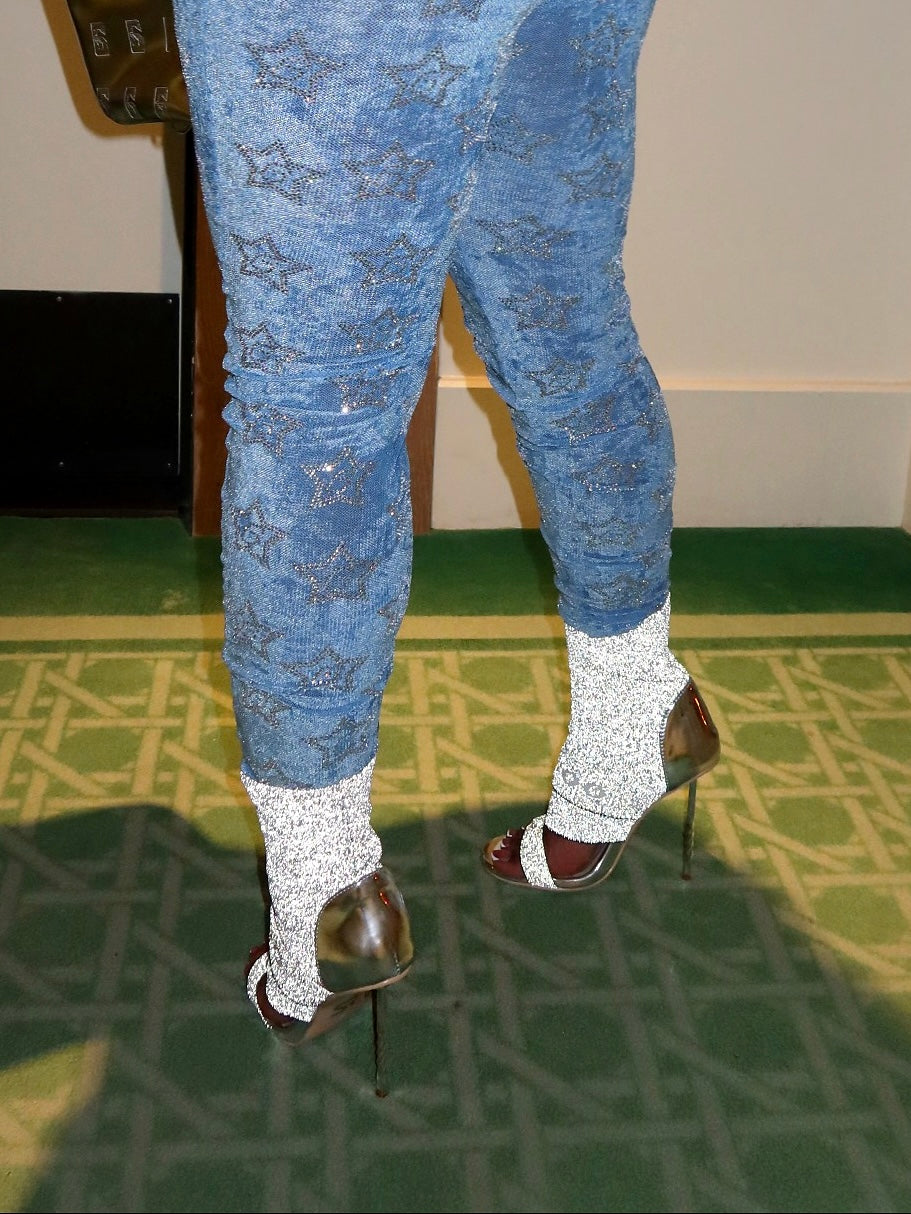 Person wearing blue patterned pants and high-heeled shoes on a green carpet.