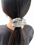 Person with a gray scrunchie with silver chain detail in a ponytail on a white background